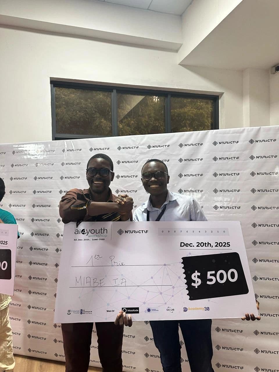 Ewan Semadegbe et Eli Jean Doumeyan tenant le chèque du premier prix de 500 $, devant le mur de presse Neuractif.